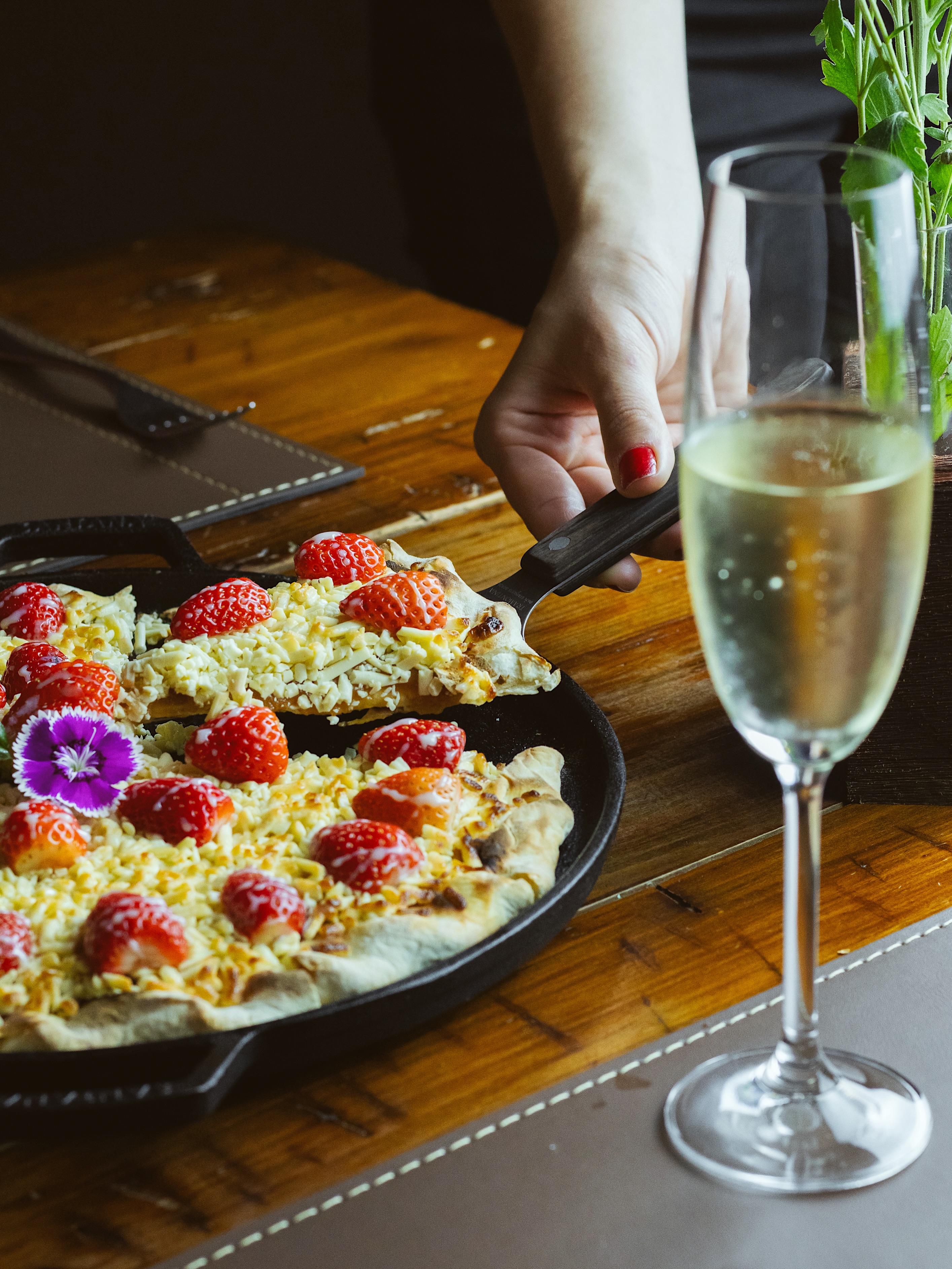 Pizza doce de morango servida na frigideira ao lado de uma taça de espumante