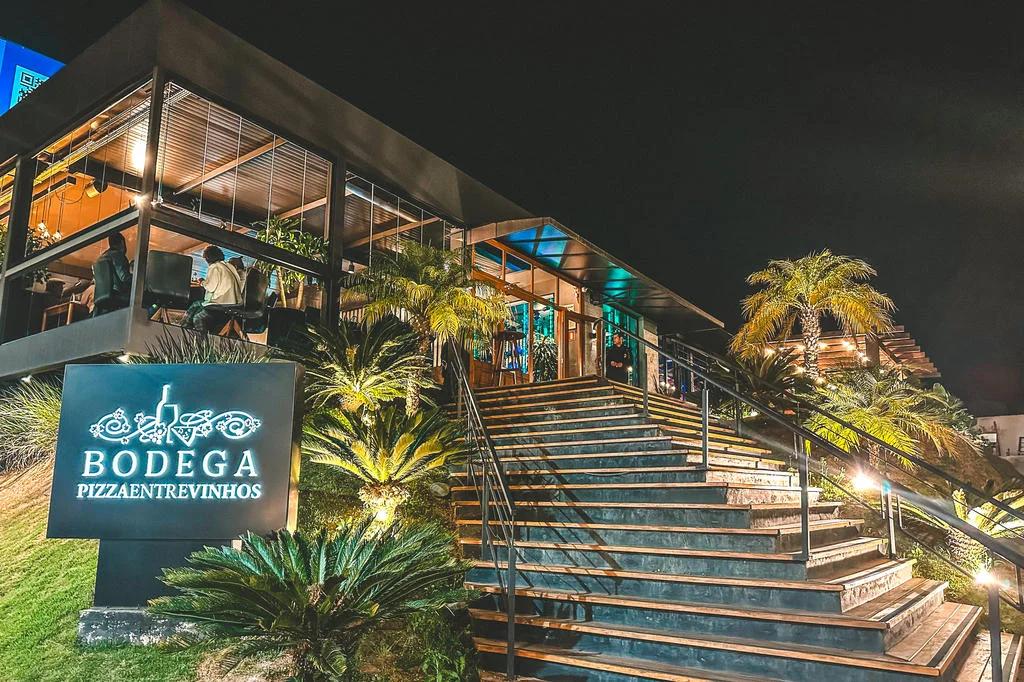 Fachada iluminada da Bodega Pizza Entre Vinhos à noite
